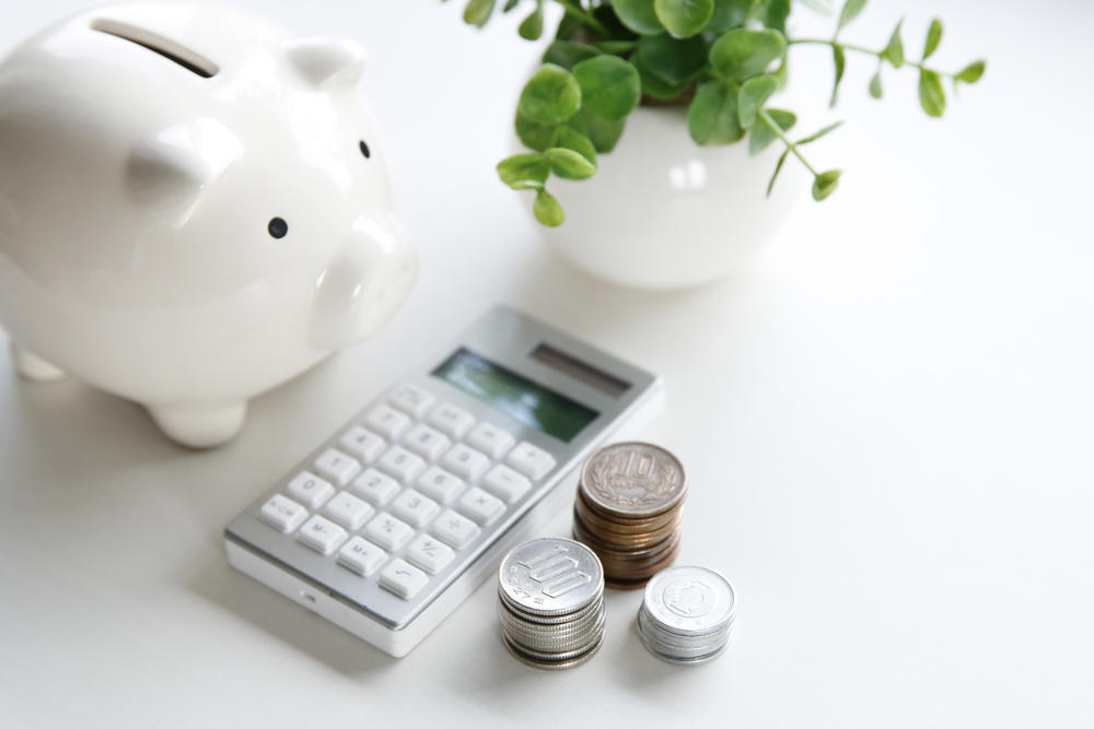 A piggy bank, hand-held calculator, desk plant and three stacks of coins.